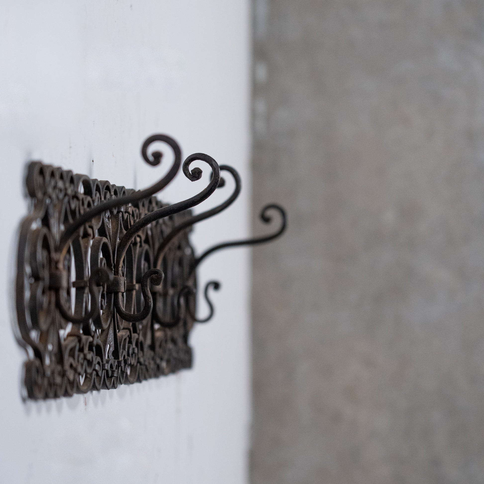 Antique French wrought iron wall rack with scrolling decorative details and aged black patina.
