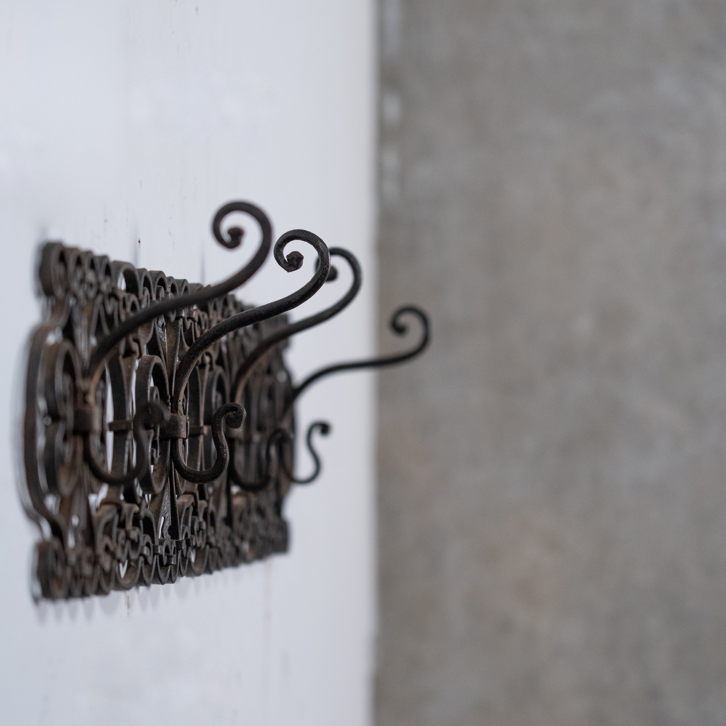 Antique French wrought iron wall rack with scrolling decorative details and aged black patina.