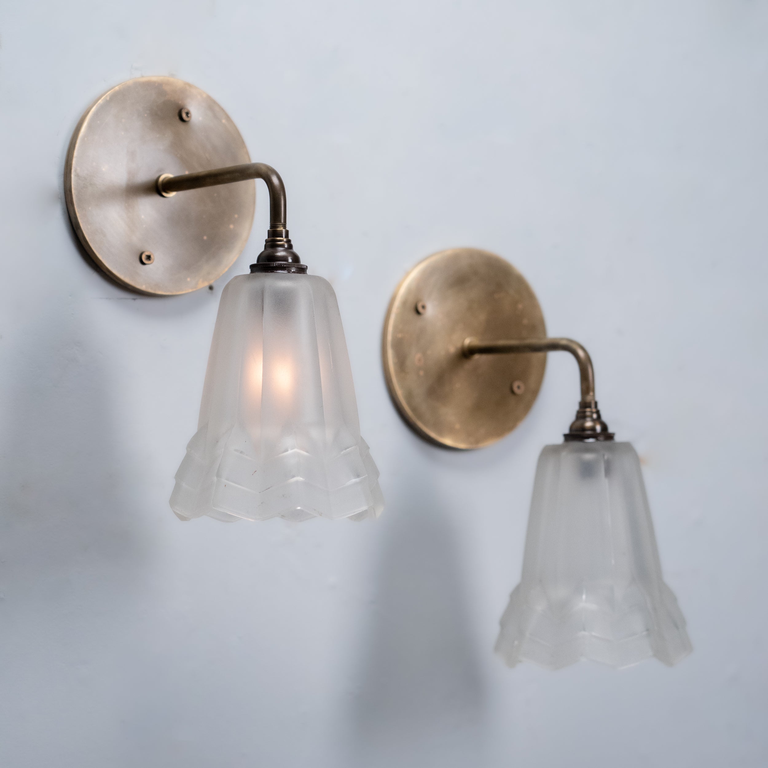 Pair of French Art Deco wall sconces with original frosted molded glass shades and brass backplates, circa 1930