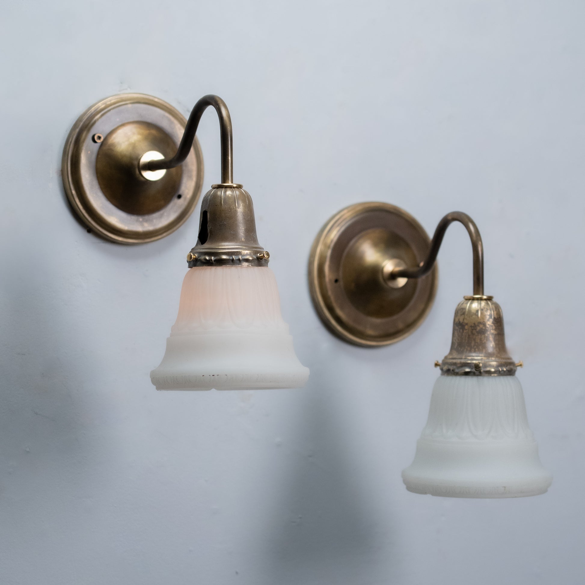 Pair of antique brass wall sconces with frosted satin glass shades and curved gooseneck arms
