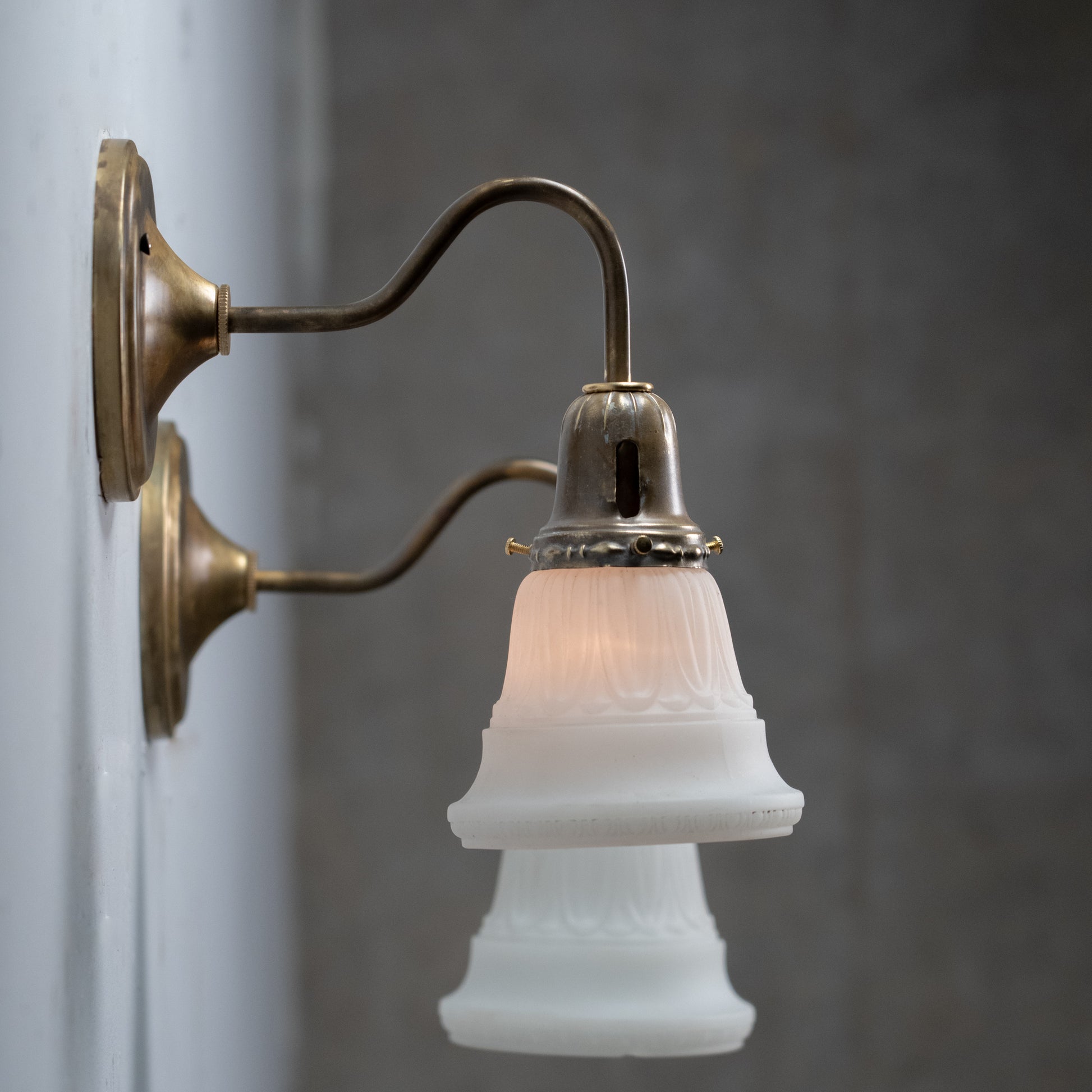 Pair of antique brass wall sconces with frosted satin glass shades and curved gooseneck arms