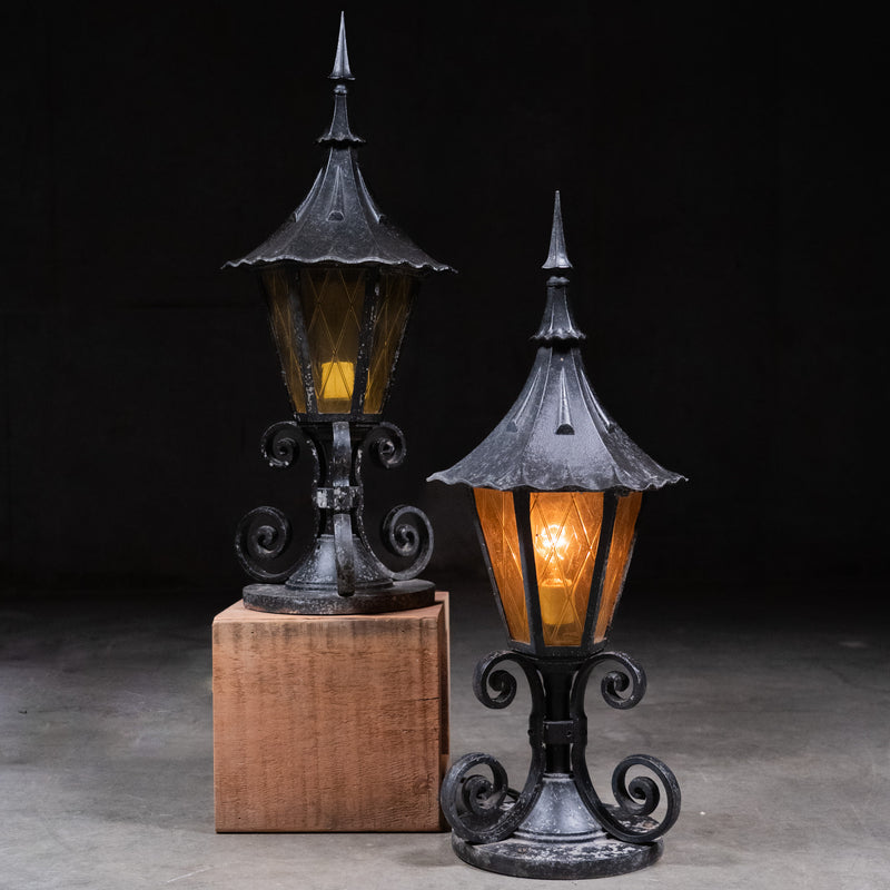 Pair of Gothic Revival outdoor post lanterns with amber textured glass panels and decorative cast metal bases mounted as garden gate and pillar lights.