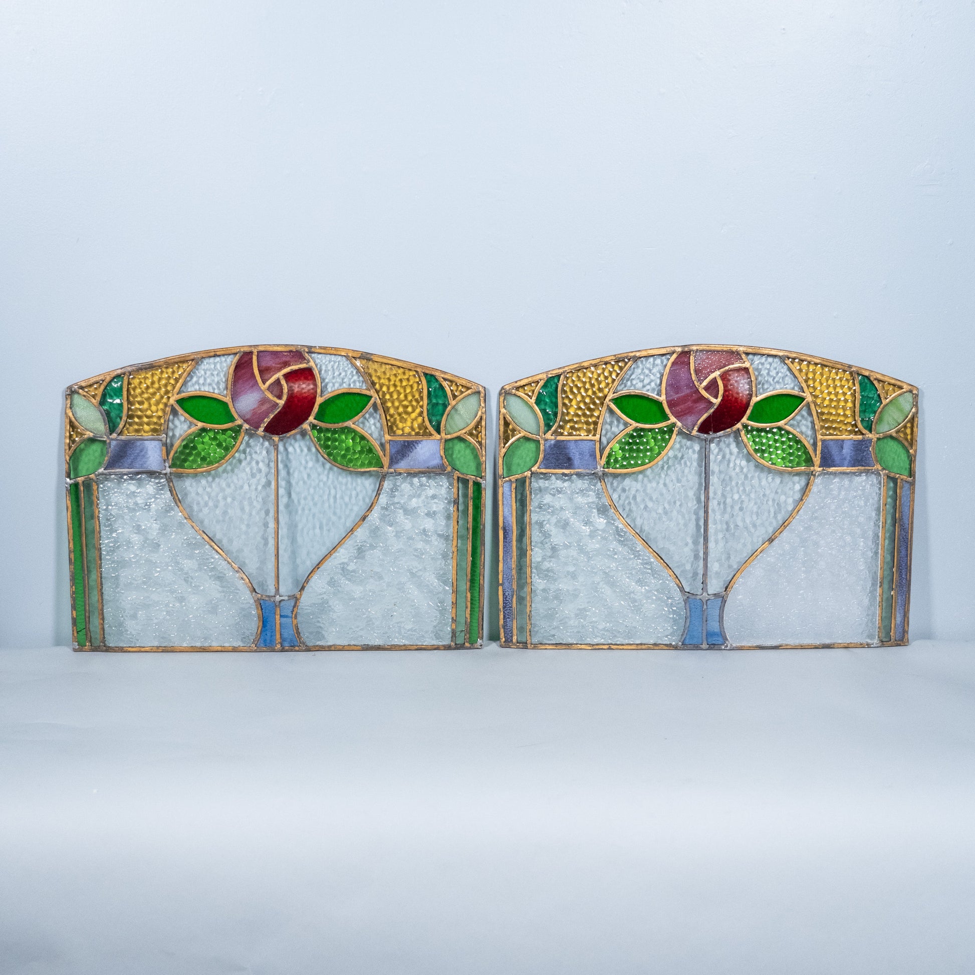 Pair of antique Art Nouveau stained glass transom windows featuring hand-leaded floral designs with textured cathedral glass, ruby, green, amber and blue art glass, circa 1900–1920.