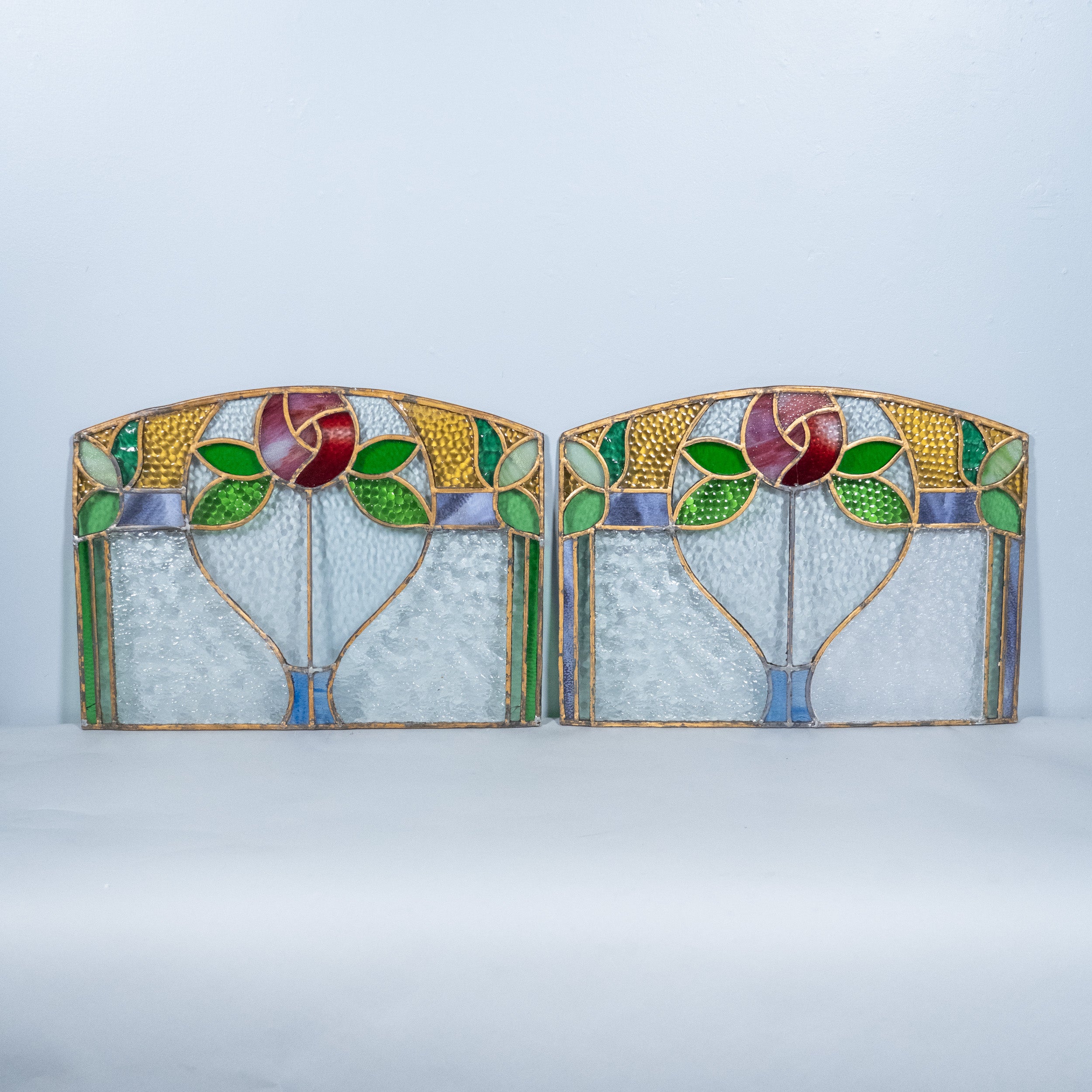 Pair of antique Art Nouveau stained glass transom windows featuring hand-leaded floral designs with textured cathedral glass, ruby, green, amber and blue art glass, circa 1900–1920.