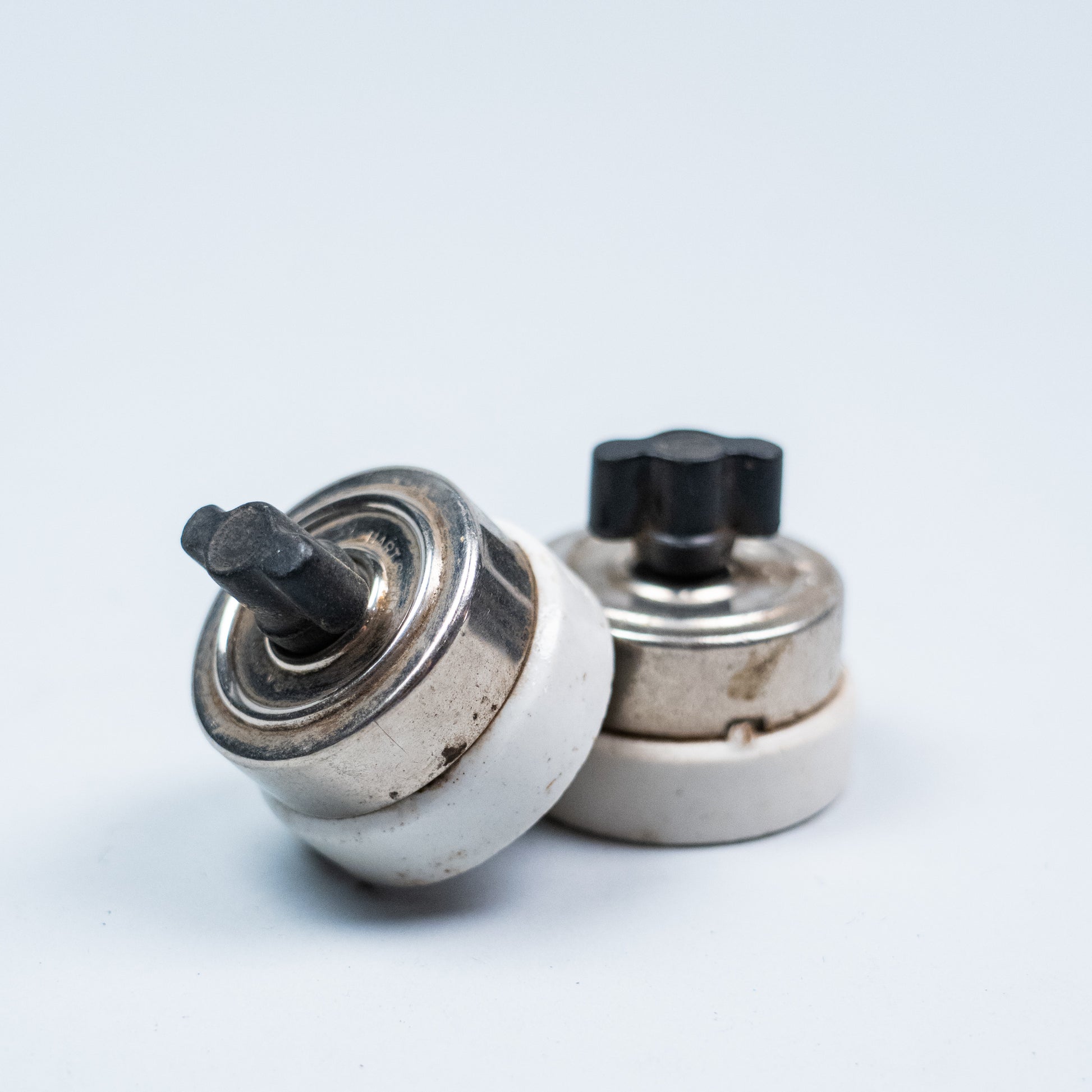 Pair of vintage porcelain push button light switches with black Bakelite buttons and nickel-plated metal housings.