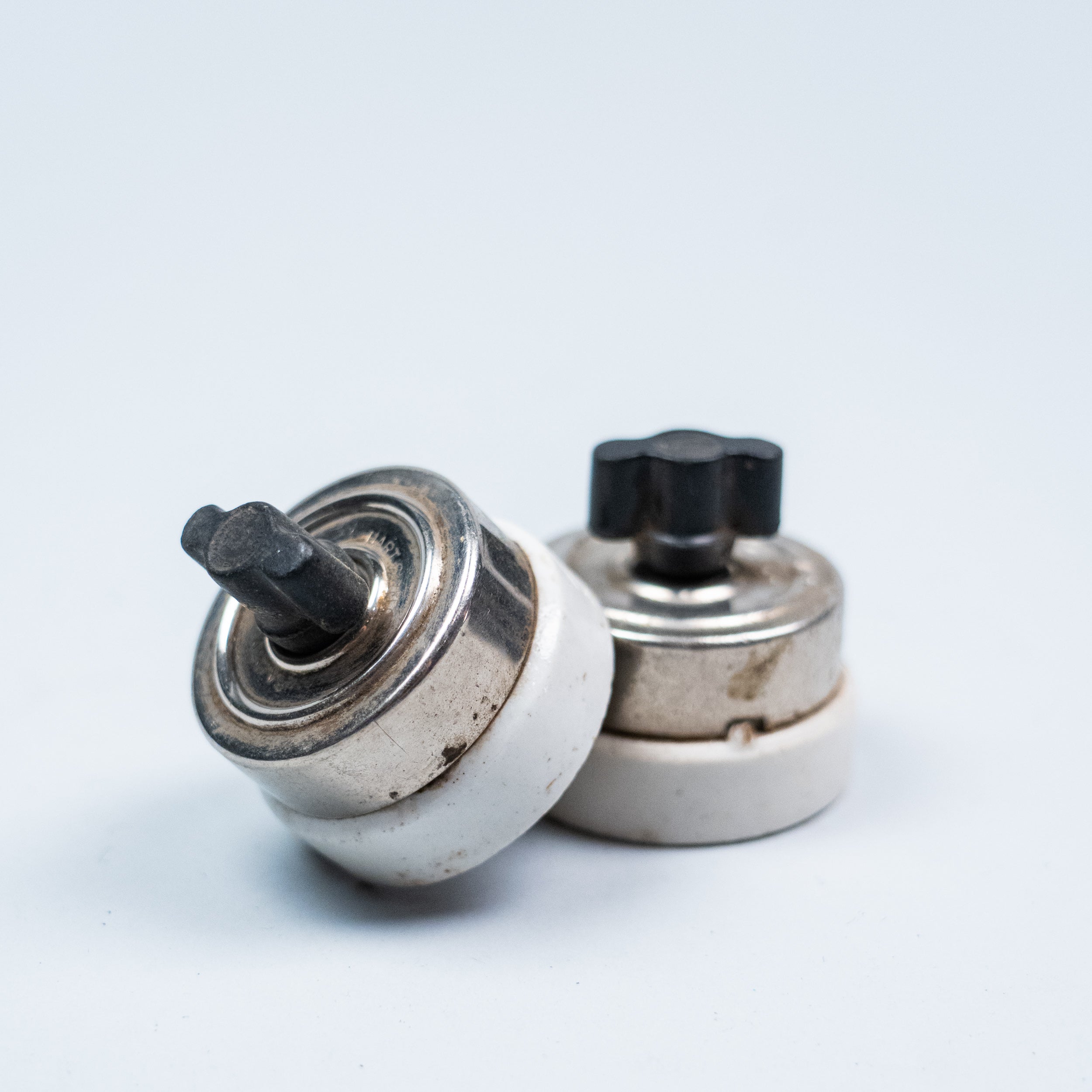 Pair of vintage porcelain push button light switches with black Bakelite buttons and nickel-plated metal housings.